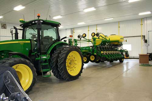 Well-lit Storage building with tractor and equipment inside has Schweiss bifold doors 